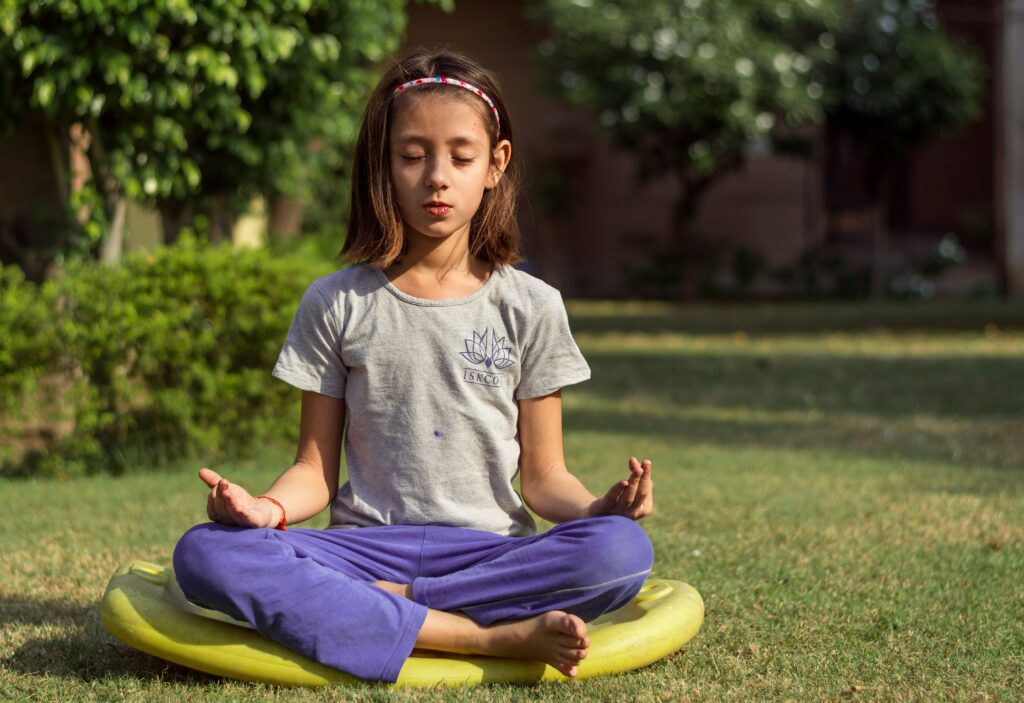 A young girl sitting outside on a mat letting go and allowing by meditating