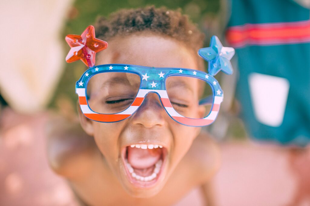 A young boy with star spangled party glasses with his head back laughing; celerbating his country.