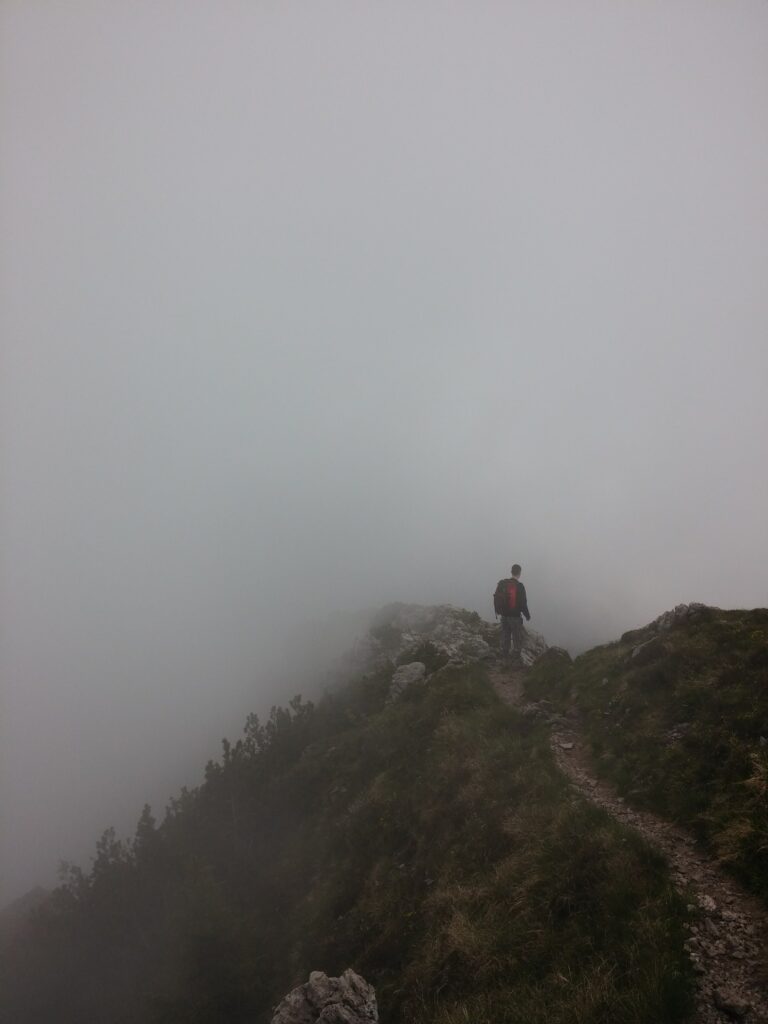 A hiker travelling a narrow rock path on a steep fog mountainside; the journey to change can be tough and full of unknowns.