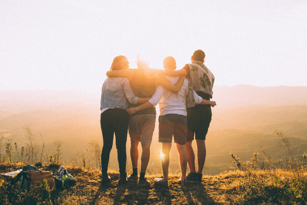 the silohuette of four friends with their arms linked tightly as they face the distant sun after having worked together to support each other through the change of altitude and aptitude.