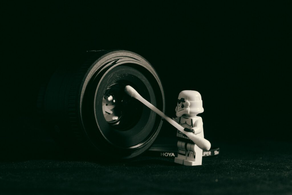  A close up of a camera lens with a tiny white starwars figure holding a QTIP- the short hand for Quit taking it Personally.