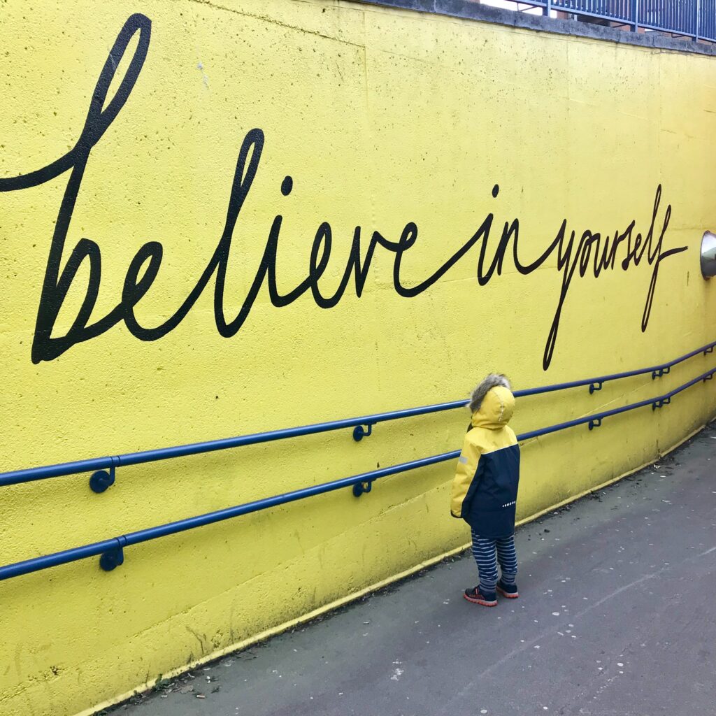 A yellow wall with big black letters that say "believe in yourself" which is the key to quit taking it personally