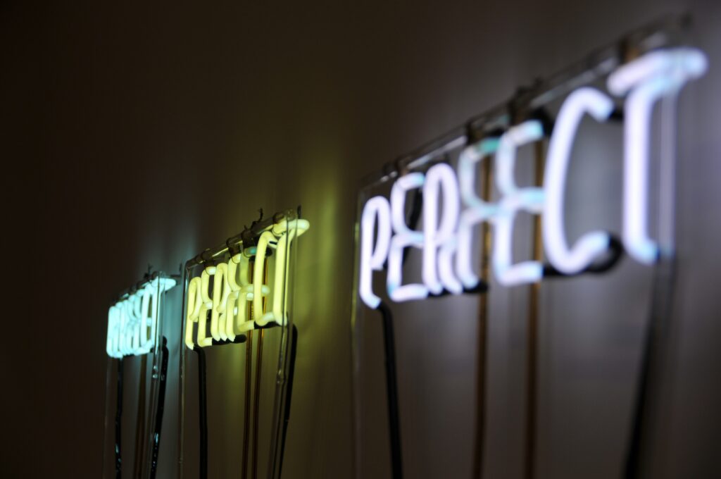 Sideview of three electric signs that say perfect which is what we are striving for when we feel like a fraud.