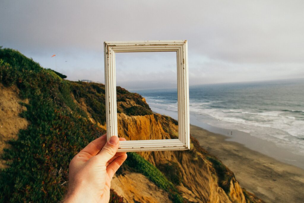A harm reaching out with a small wooden frame that captures a coastline. Reframe your limitations to see the beauty of your superpowers.