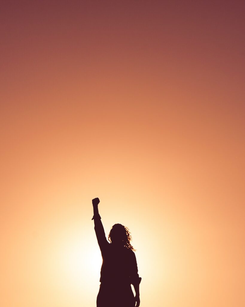 A woman silhouetted ina dusk horizon with fist in the air as she claims and names her superpower.