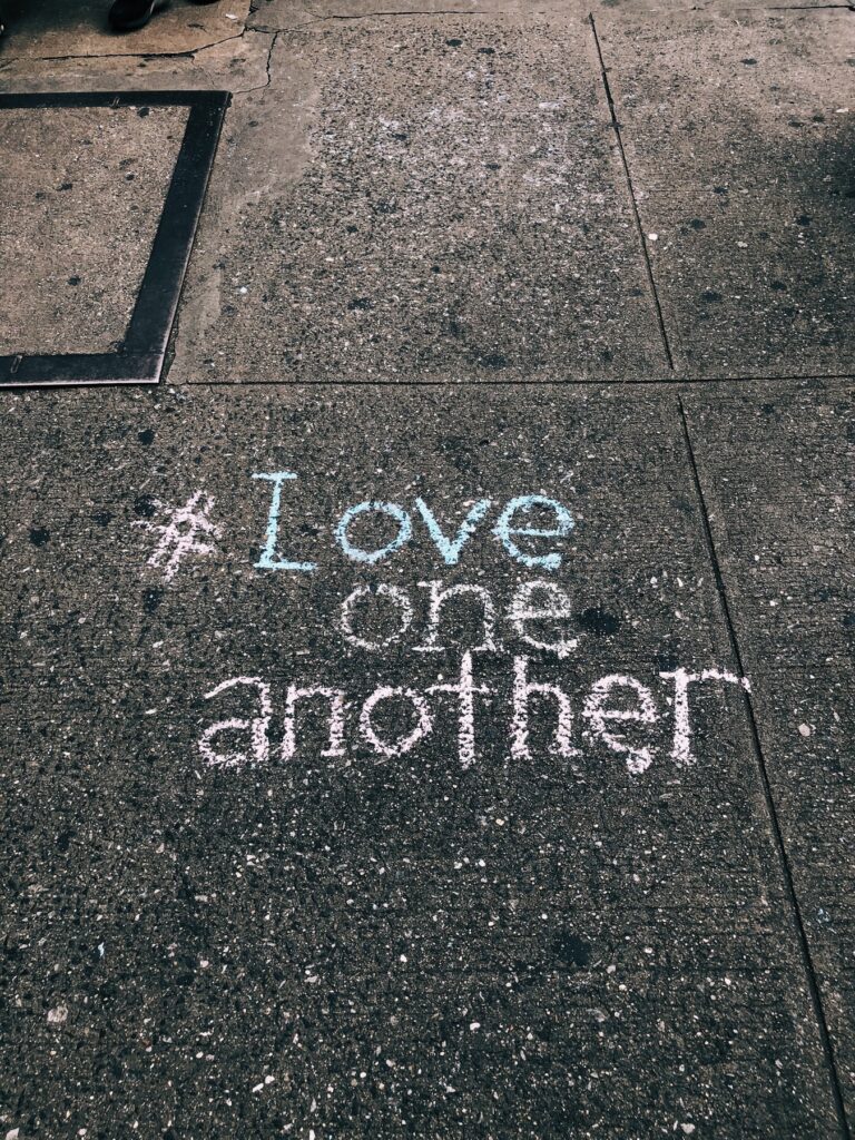 Sidewalk with #Love one another written in sidewalk chalk.