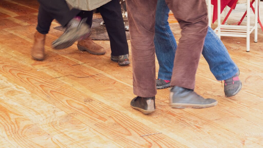 A snapshot of two pairs of feet in the midst of dancing; as one person's leg moves back, the other's moves forward.