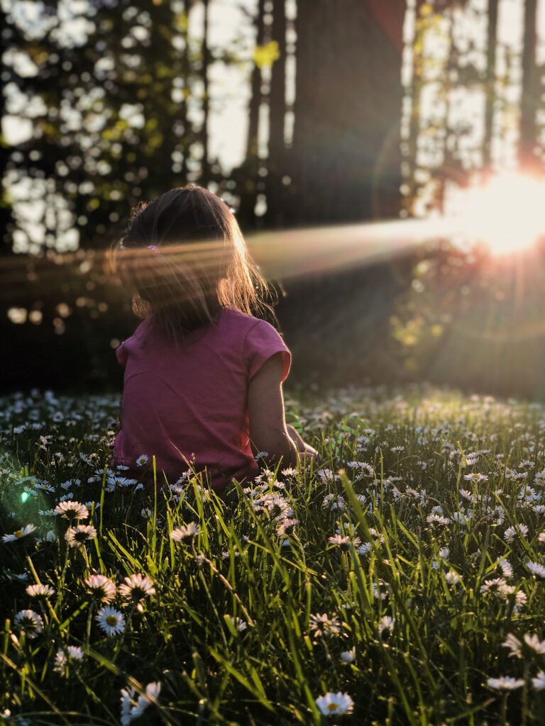A little girl sitting still in a field facing the sunshine