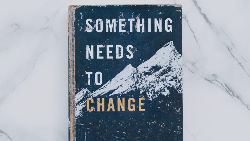 A wooden sign of a mountainscape with the words "Something Needs to change" emphasizing the need to communicate clearly about the boundaries you are setting.