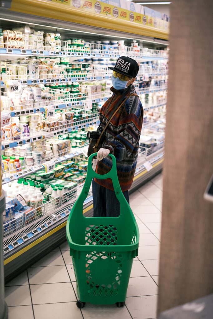 A woman in a grocery store with protective gear on. There is no way of telling what are the feelings behind the mask.