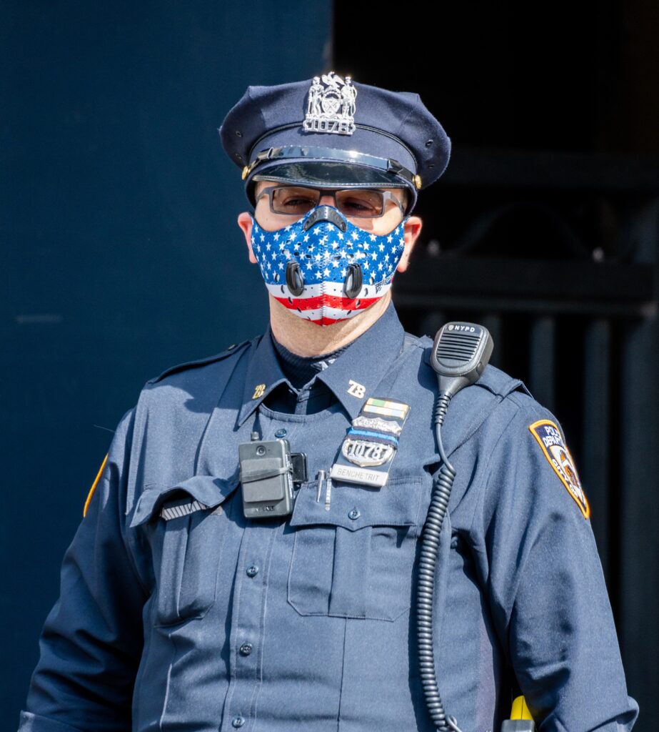 Uniformed police officer on the street with an american flag nose & mouth covering