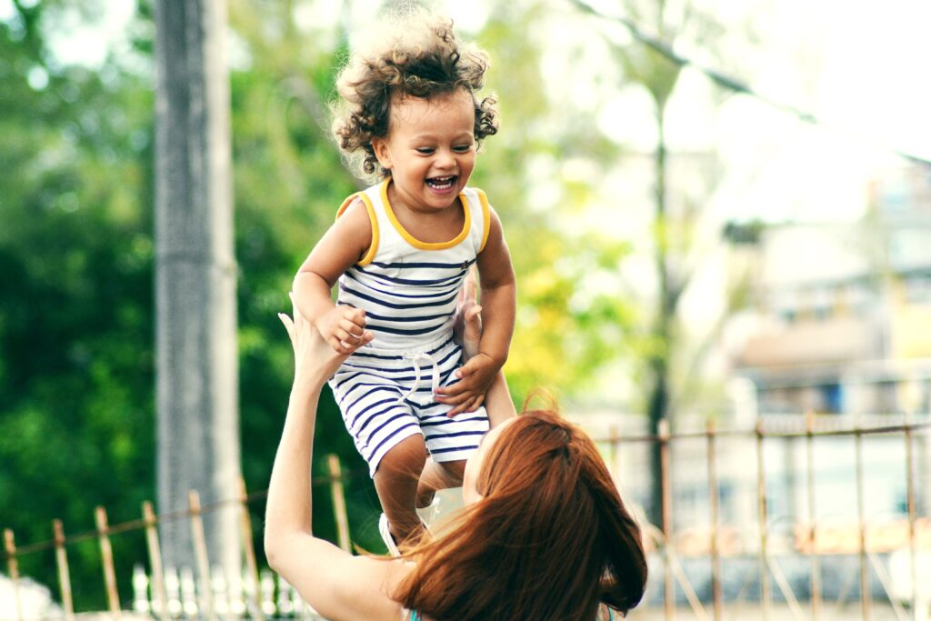Young mother helping her child cope by playfully throwing child up in the air. The child is smiling and laughing.