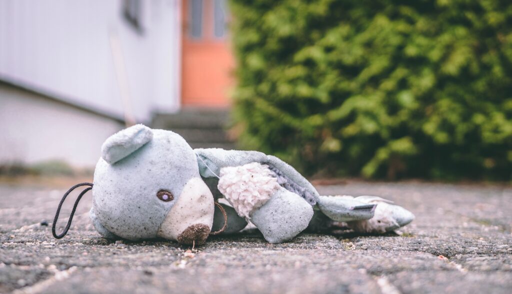 A child's lost dirty, wet and bedraggled blue and white stuffed animal face down on cobblestone.