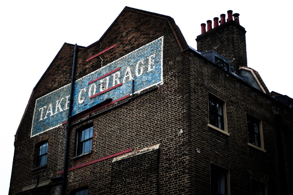A red brick building with "Take Courage" emblazoned with large white letters on blue background. We need to take courage to shape a new normal. 