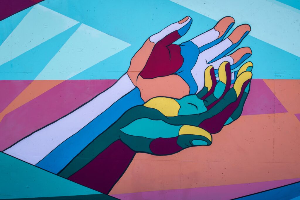 Two different multi-colored hands reaching out together in the same direction to help shape a new normal