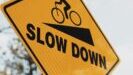 Yellow street sign with bike going down hill that says SLOW DOWN insisting adjusting course