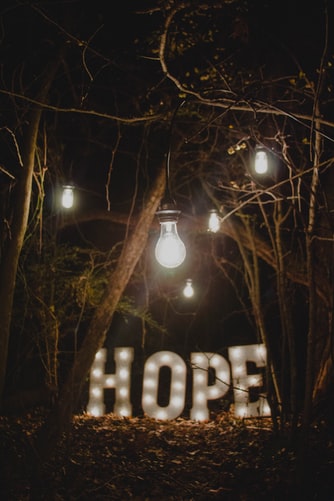 Metallic Hope letters lit up in the dark woods. There is hope for what's wrong with you.
