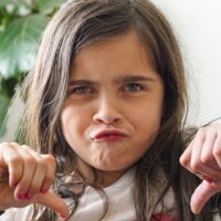 A young girl with a defiant face and her thumbs down 