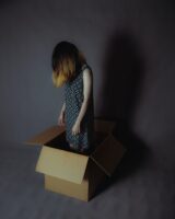 Woman stuck standing inside a box with head down and shoulders slumped. 