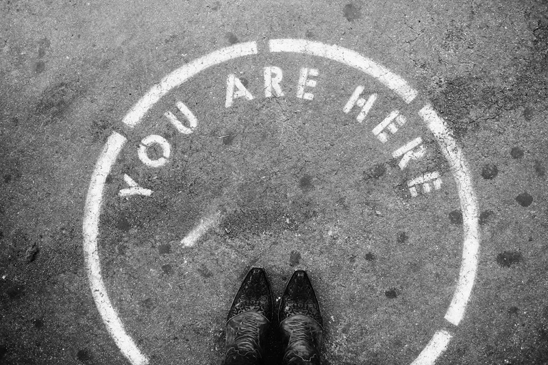 Black boots at the bottom of a white circle with the words ‘you are here’ You have arrived.