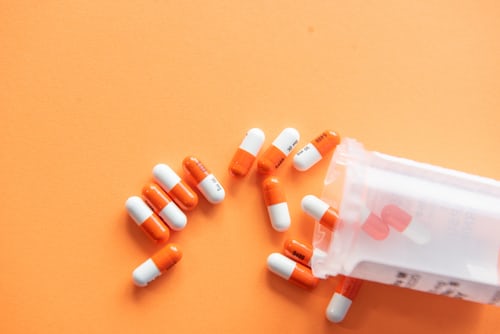 A prescription bottle with orange and white pills spilled out onto orange background. Medicine brought the author significant relief on her journey towards diagnosis