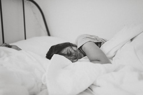An exhausted woman asleep on a bed of tumbled white sheets and comforter