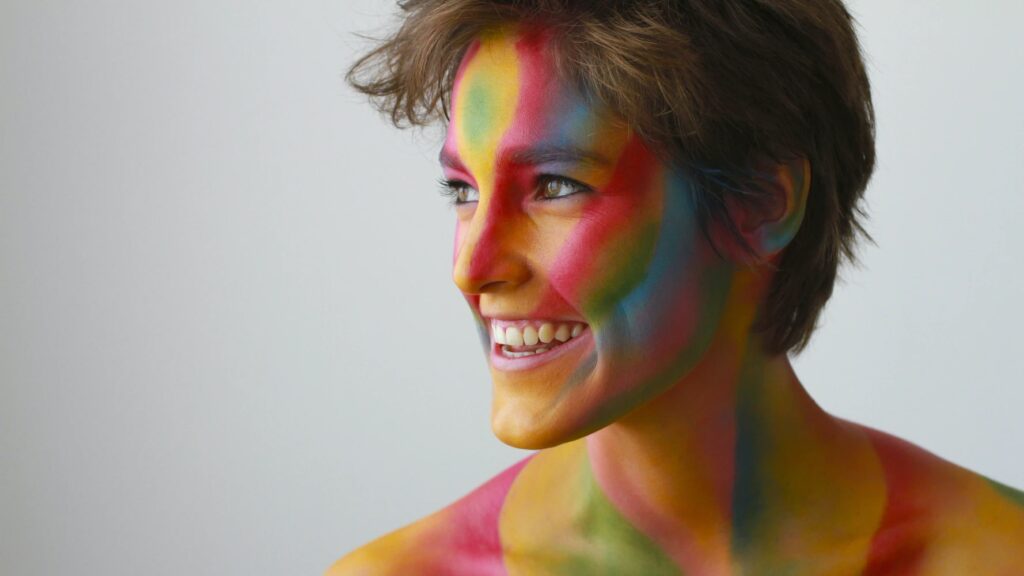 Smiling woman shining her light with bold, bright colors painted on her face and shoulders