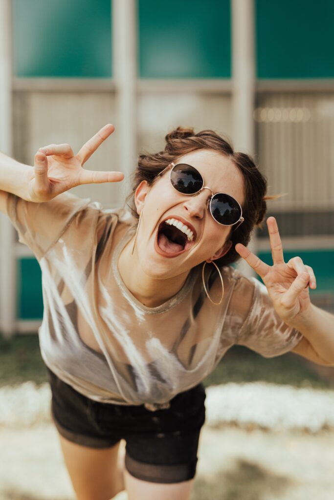 Happy Woman leaning into camera with sunglasses and big smile. She’s celebrating Her wholeness.