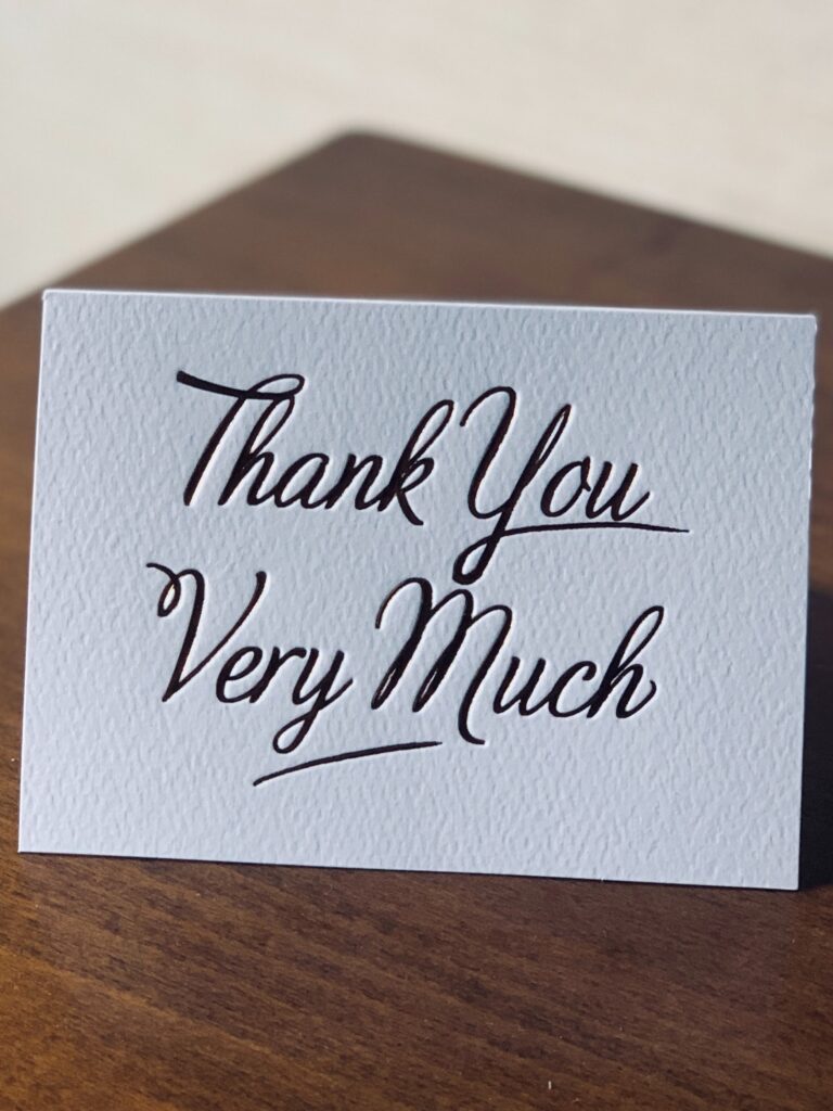 A white note card with "thank you very much" on the front.