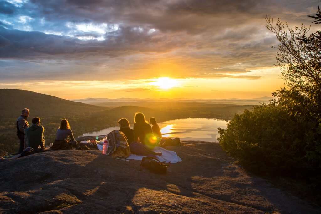 Friends gathered at sunset on a mountaintop overlooking a lake
