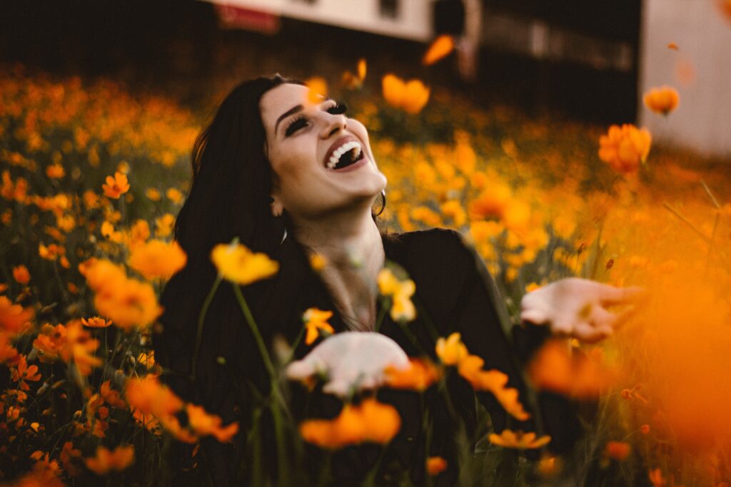 A woman laughing and tossing flowers in the air as she kneels in a field of poppies