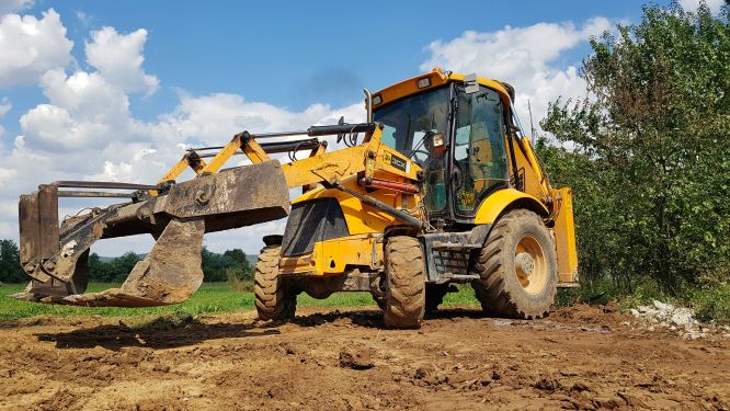 A large yellow landscape vehicle with front loader leveling the dirt in a field