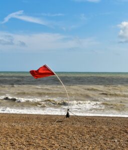 A Red Flag blowing in a gusty wind on the shoreline of a turbulent sea