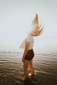 Woman shin deep in water flipping hair so it looks like here head is the sun