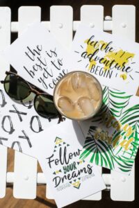 Ice coffee and sunglasses over cards that say follow your dreams, let the adventure begin, and the best is yet to come.
