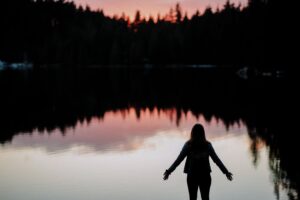 A women surrendering to the miracle of the sunset over a forested lake